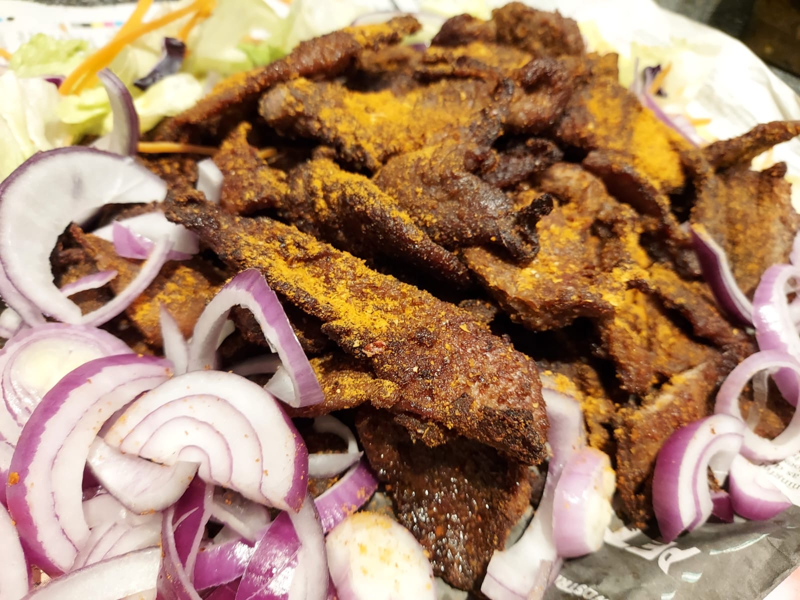 Plate of spiced beef suya with sliced red onions and salad